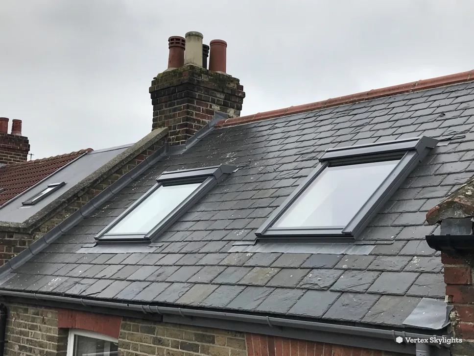 Two roof windows in an old slate roof beside a chimney
