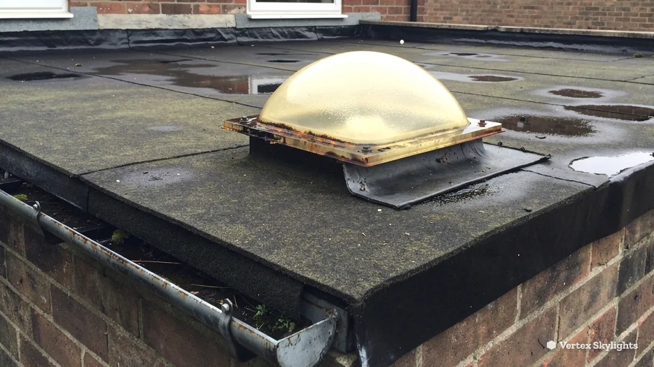 An old yellowed plastic dome rooflight on a worn flat roof