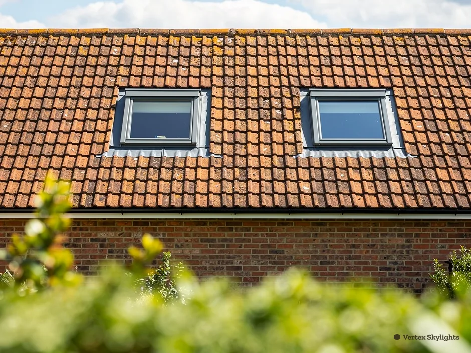 Two roof windows in an orange clay tile roof above a hedge