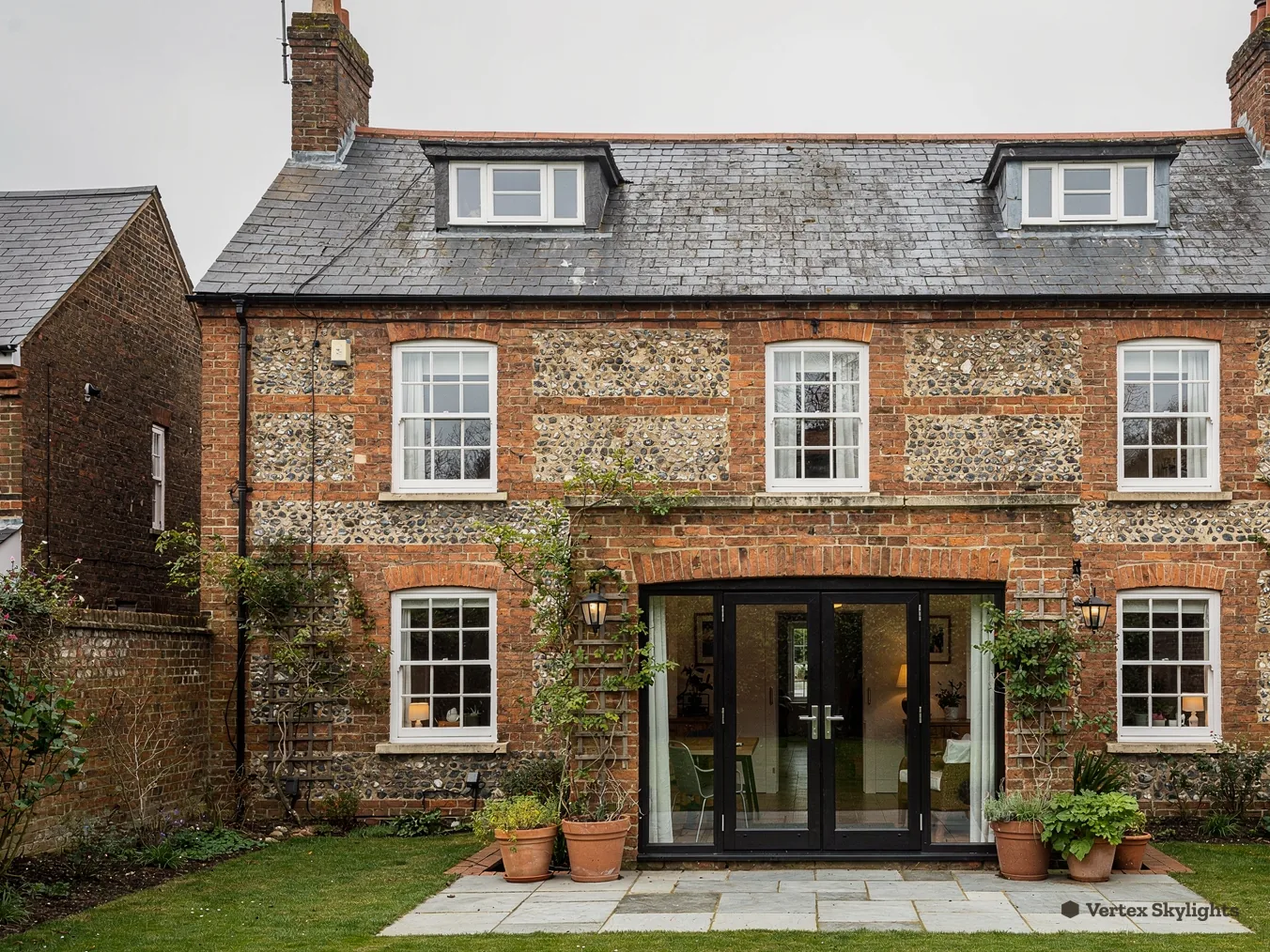 A stone and brick house with roof windows in its slate roof and a garden in front