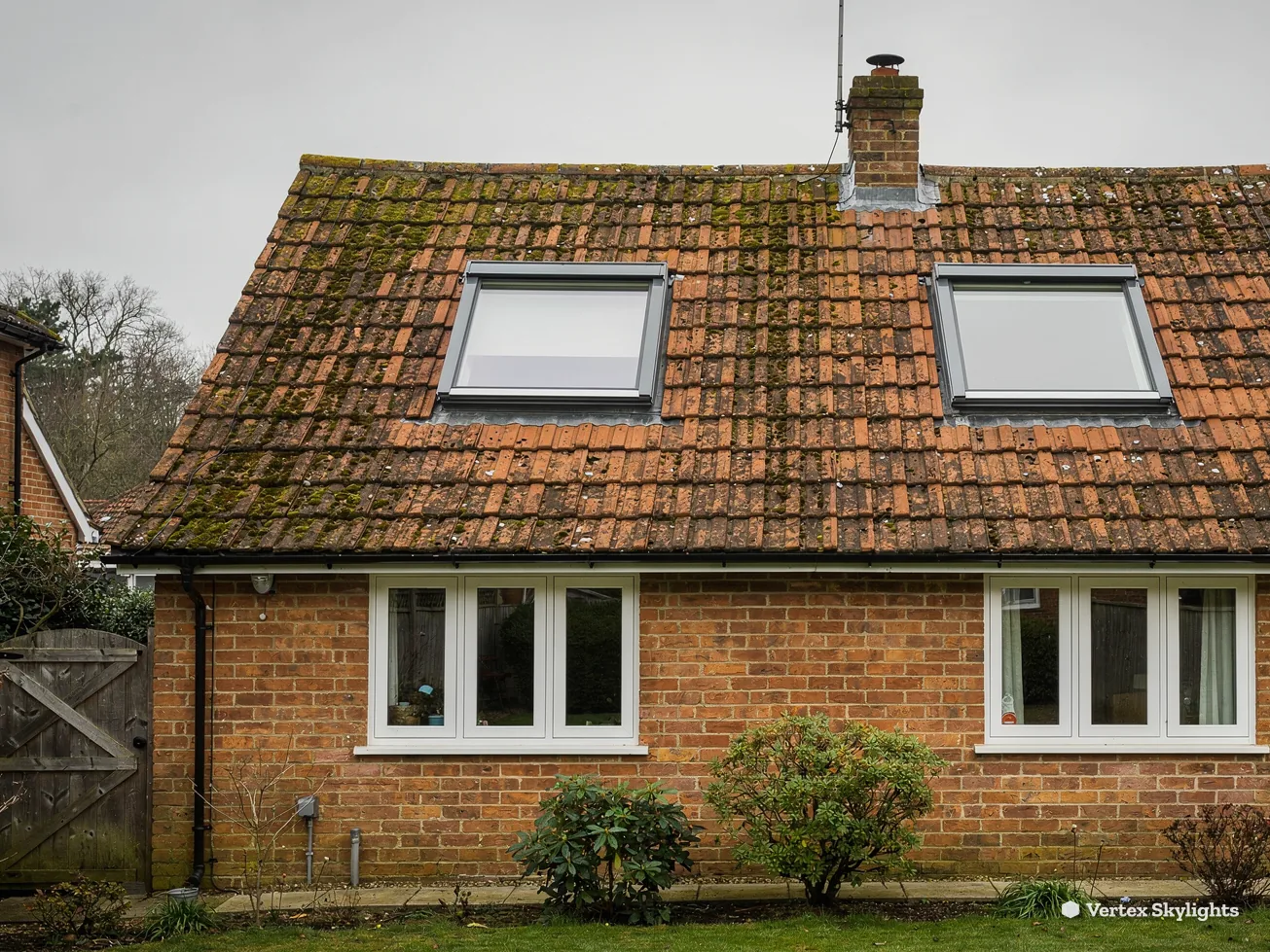 A brick cottage with two roof windows in a mossy tiled roof