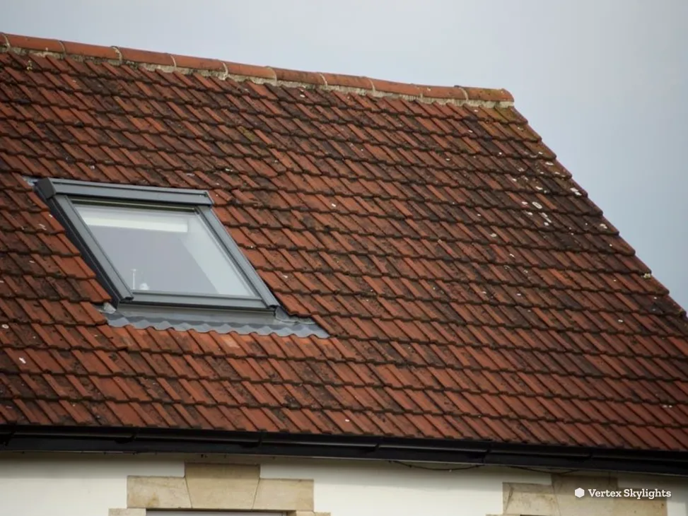 A roof window in a red clay tile roof against the sky