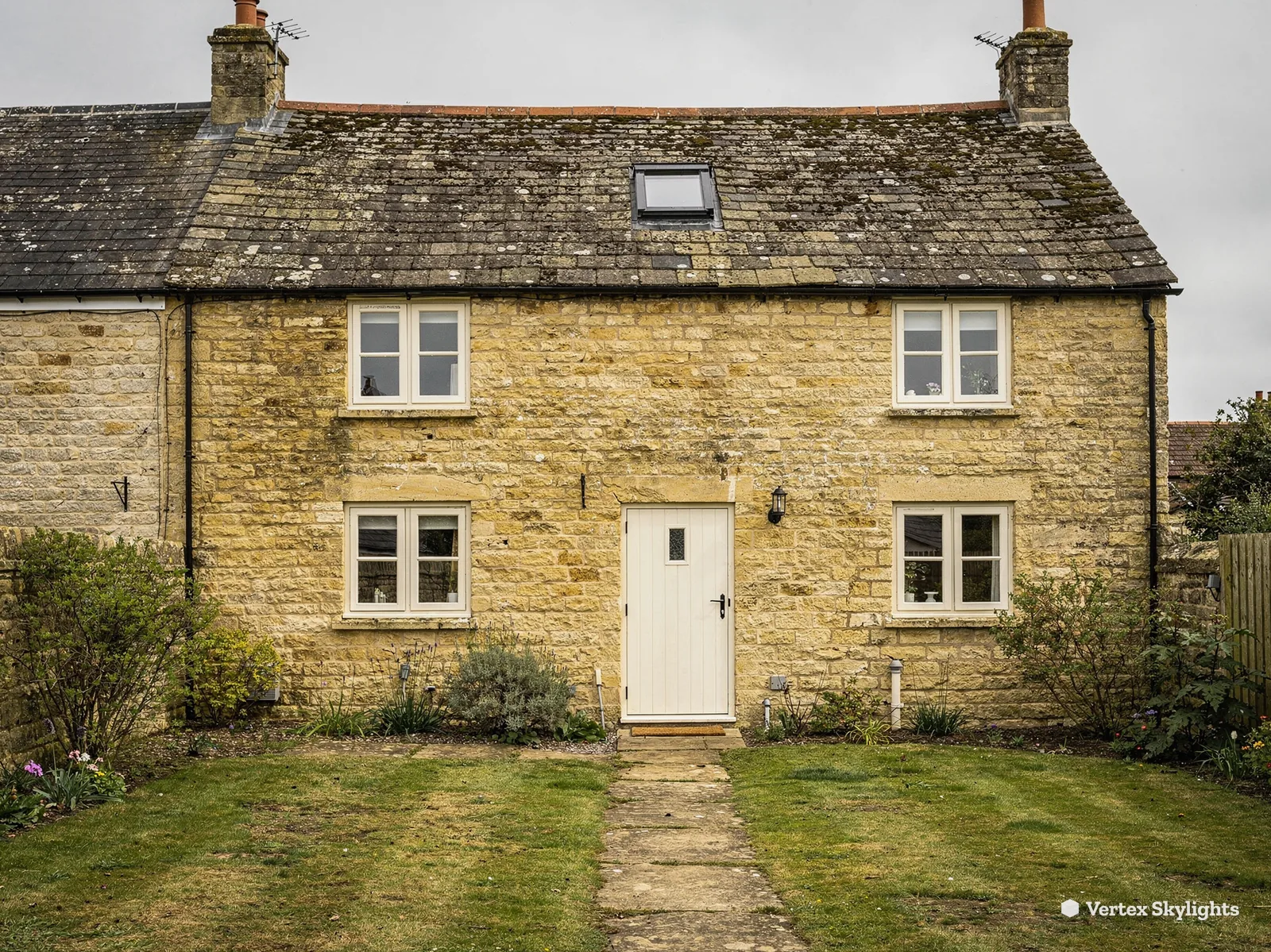 A stone cottage with a small rooflight in its stone slate roof, a path through the lawn
