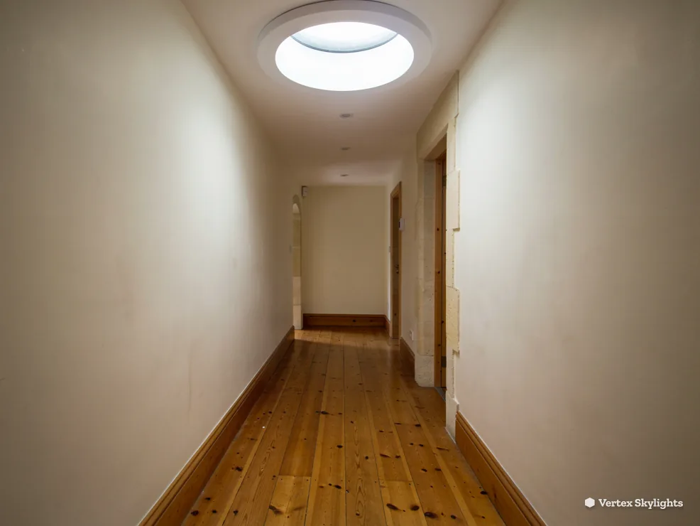 A narrow hallway lit by a sun tunnel diffuser in the ceiling