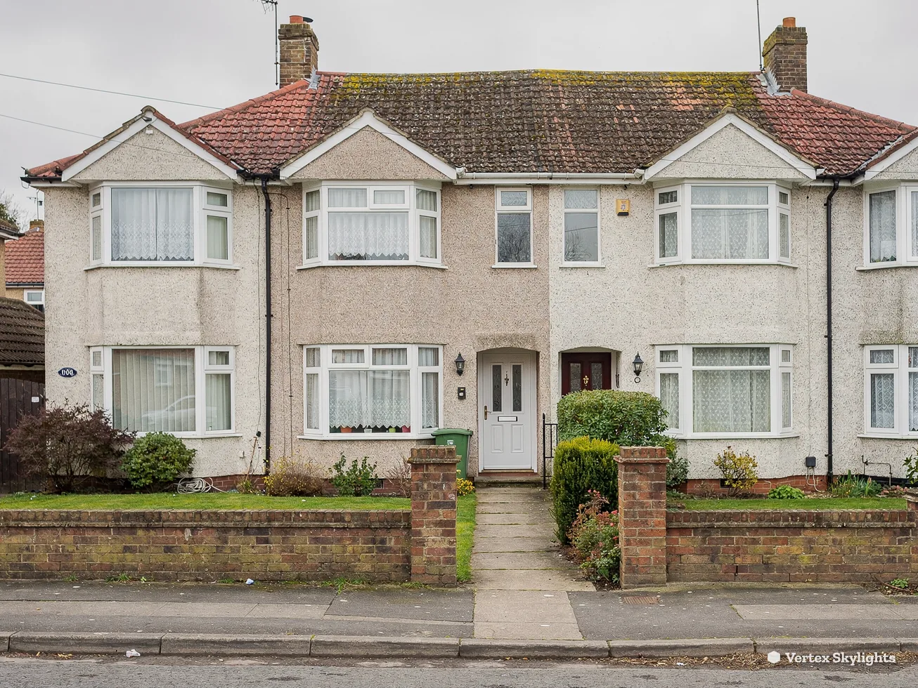 A pair of rendered 1930s semis with tiled roofs behind low walls