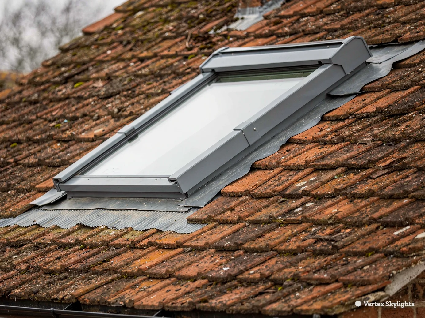 A roof window with grey flashing in a clay tile roof