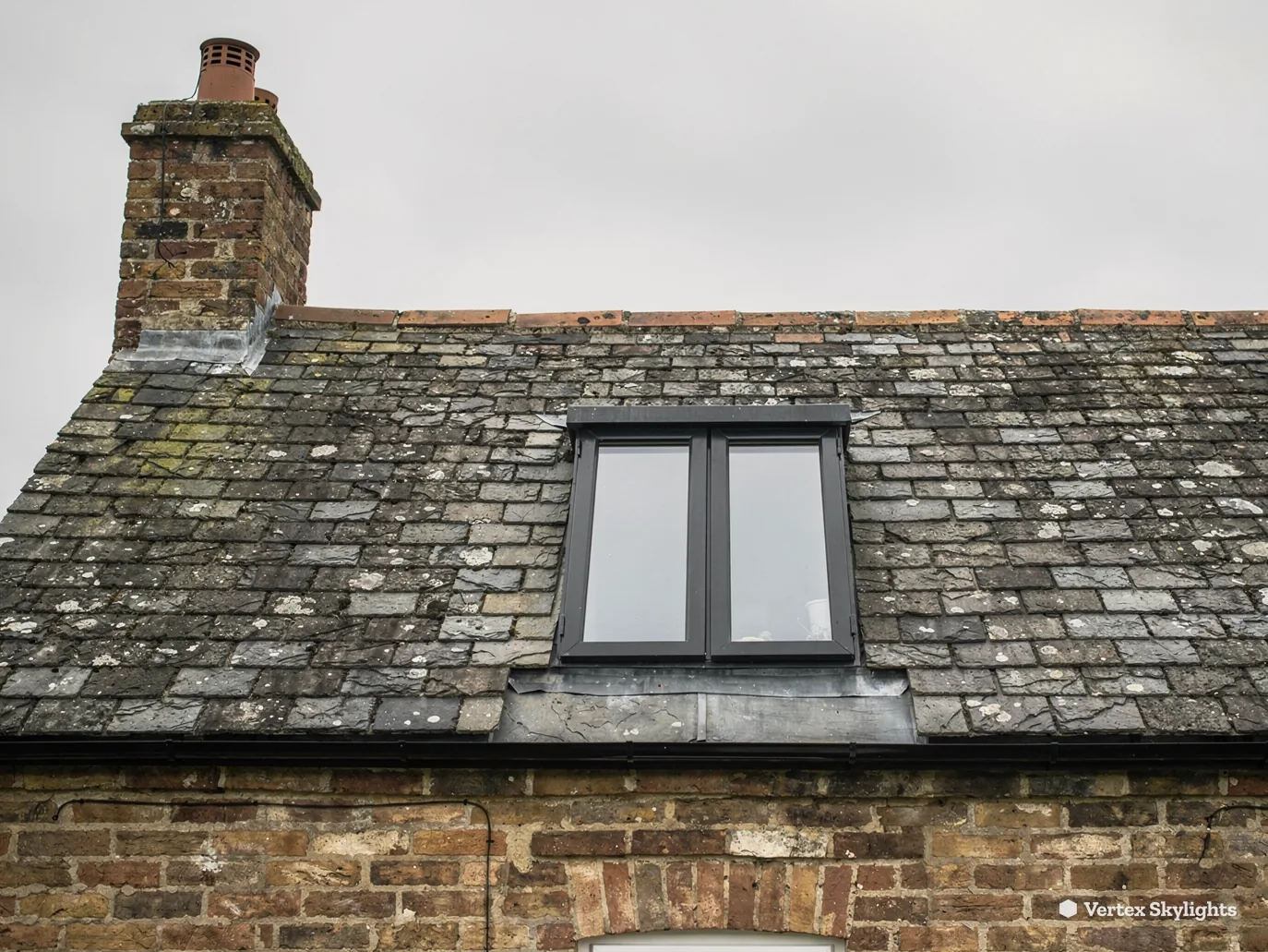 A roof window in an old slate roof over brick walls